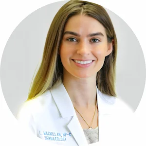 A person with long hair, wearing a white lab coat with "Dermatology" written on it, smiles at the camera.