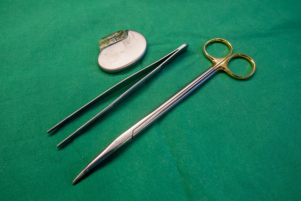 Surgical instruments including scissors, a pair of tweezers, and a needle holder on a green cloth.