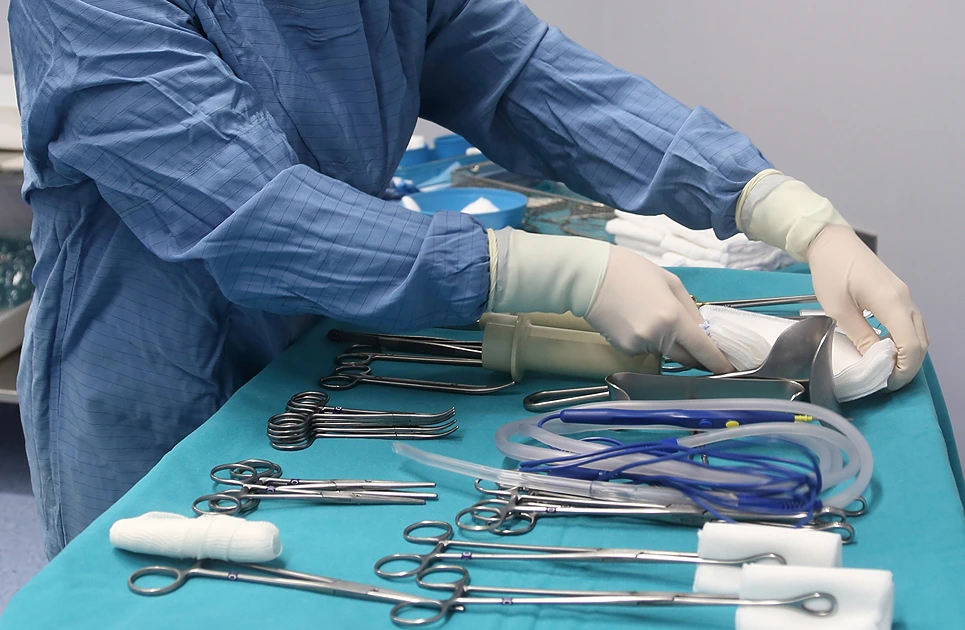 A healthcare professional in blue scrubs prepares surgical tools on a table, with a focus on glove-covered hands organizing equipment.