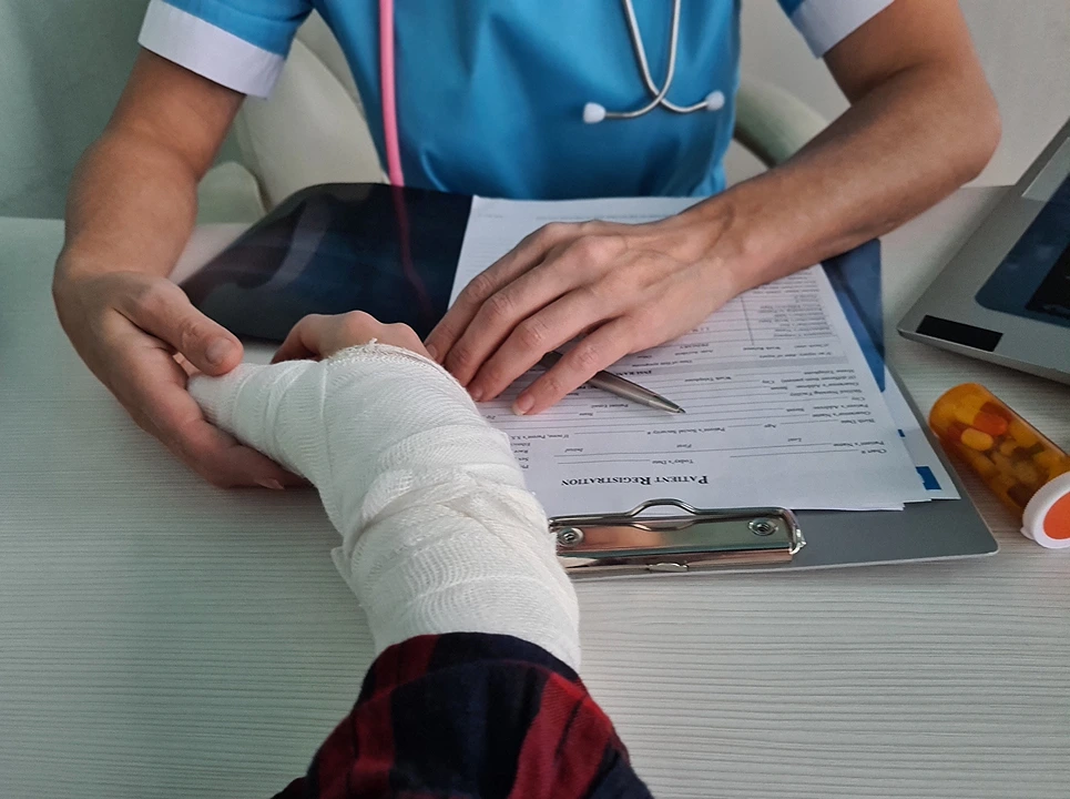 A healthcare professional examining a patient's bandaged arm at a desk with medical paperwork.