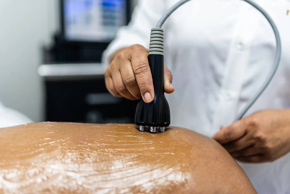 Person using an ultrasound cavitation device on a person's back in a clinical setting.