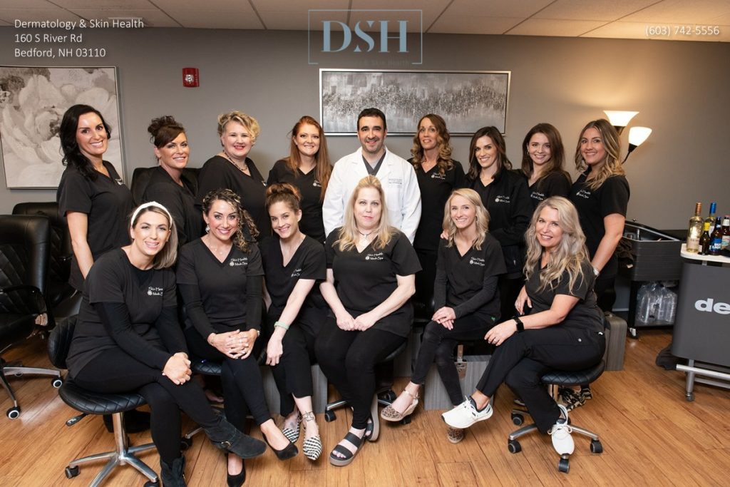 A group of healthcare professionals, including 14 women and 1 man, are posing for a group photo in a dermatology clinic. They are wearing black scrubs. The logo "DSH" and clinic details are visible above them.