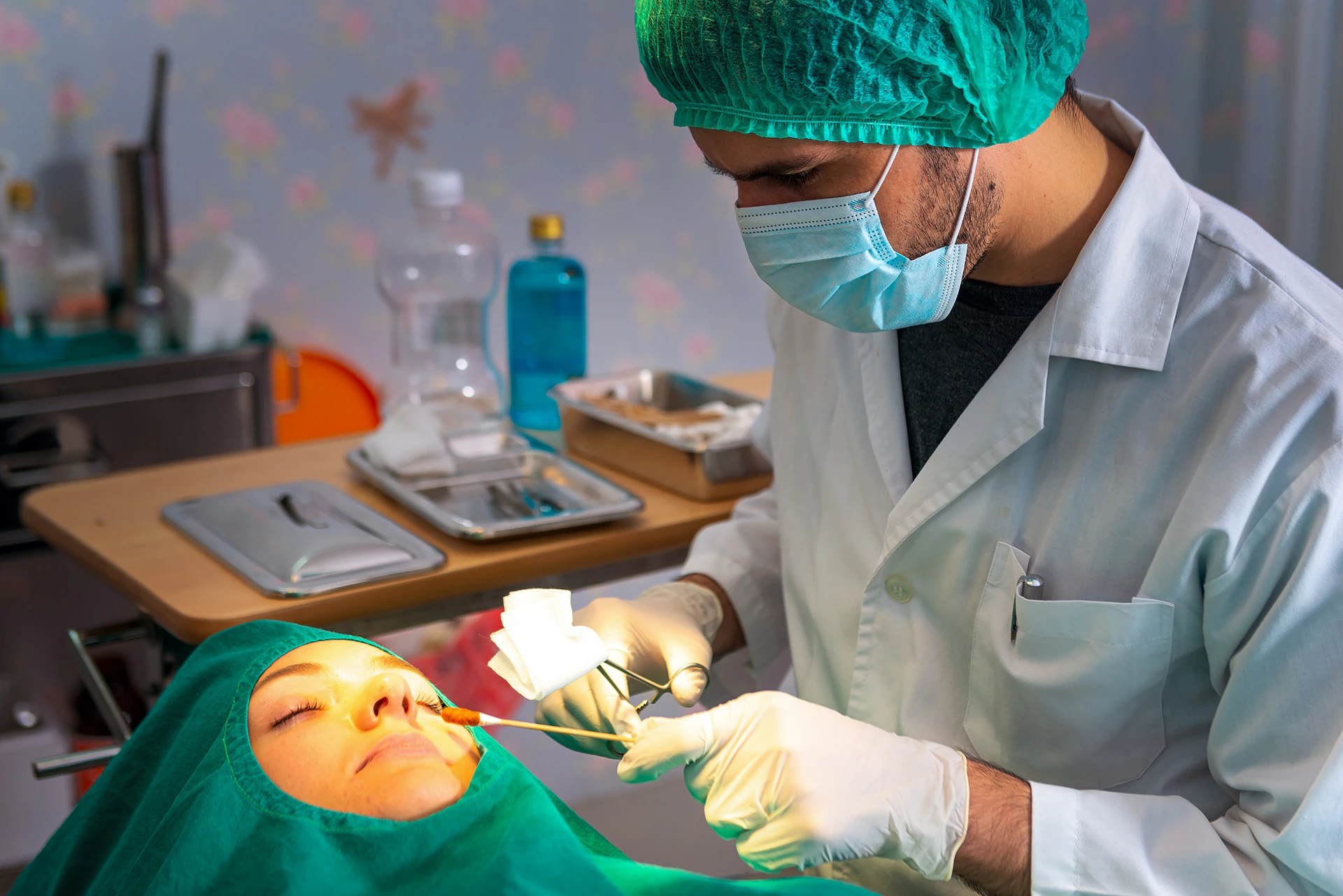 A healthcare professional in protective gear performs a procedure on a patient's nose in a clinical setting.