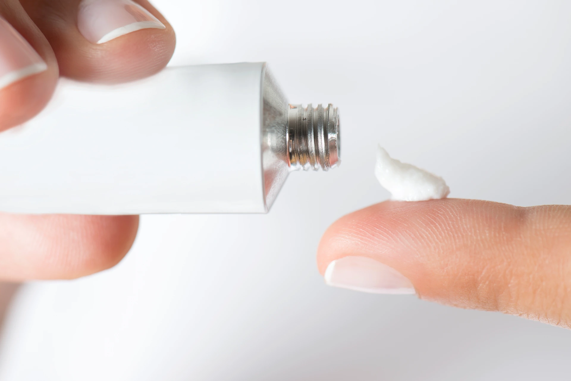 Close-up of a person's hand squeezing a small amount of white cream from a tube onto their fingertip.