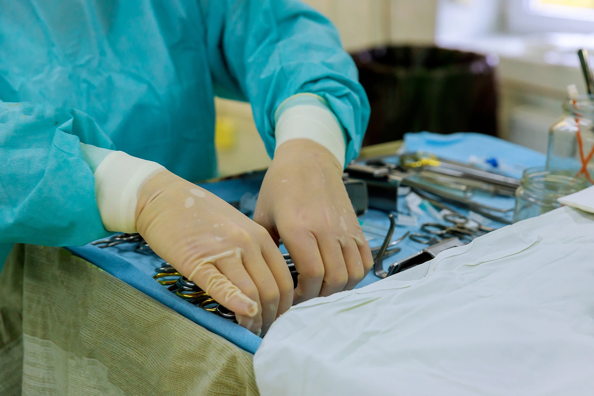 A medical professional wearing gloves and a gown organizes surgical instruments on a sterile drape in a medical setting.