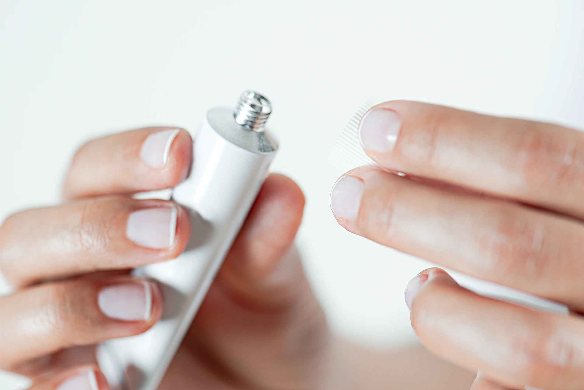 A pair of hands, one holding an open white tube and the other holding the removed cap.