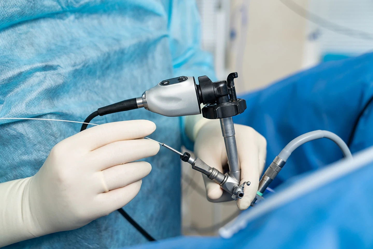 A surgeon uses an endoscope in a sterile environment, wearing blue surgical attire and gloves.