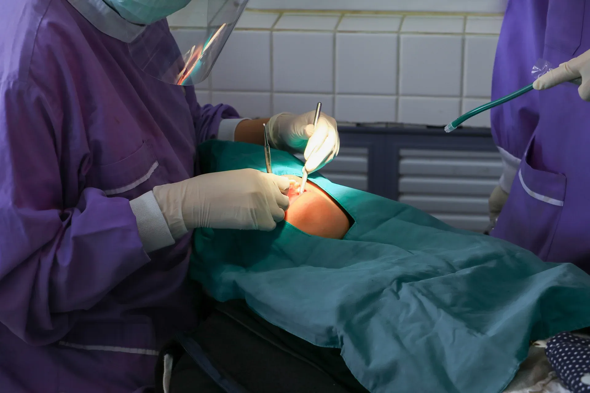 Two medical professionals in protective gear perform surgery on a patient in an operating room.