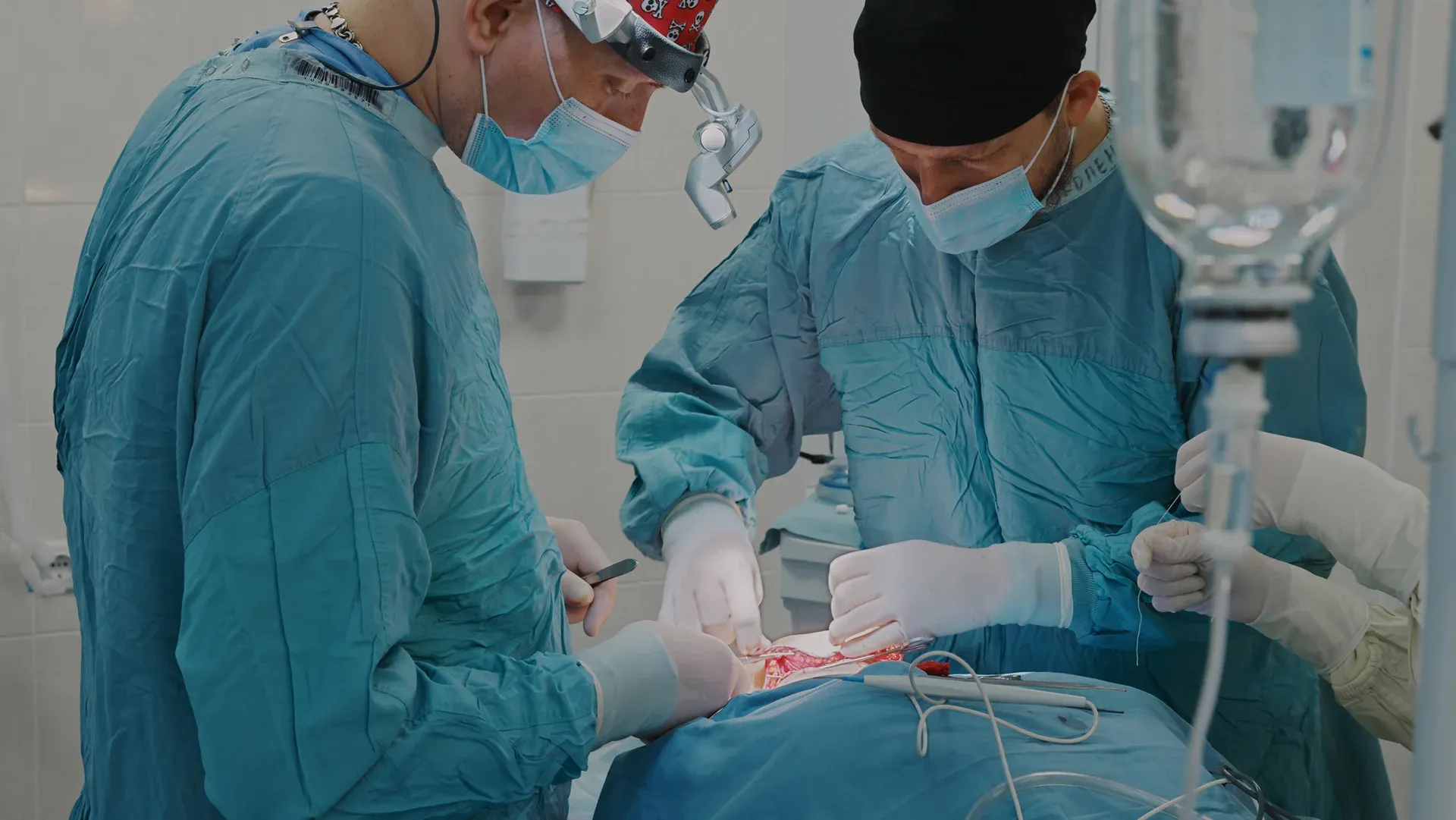 Surgeons in blue scrubs perform an operation, focusing intently on the patient, surrounded by medical equipment.