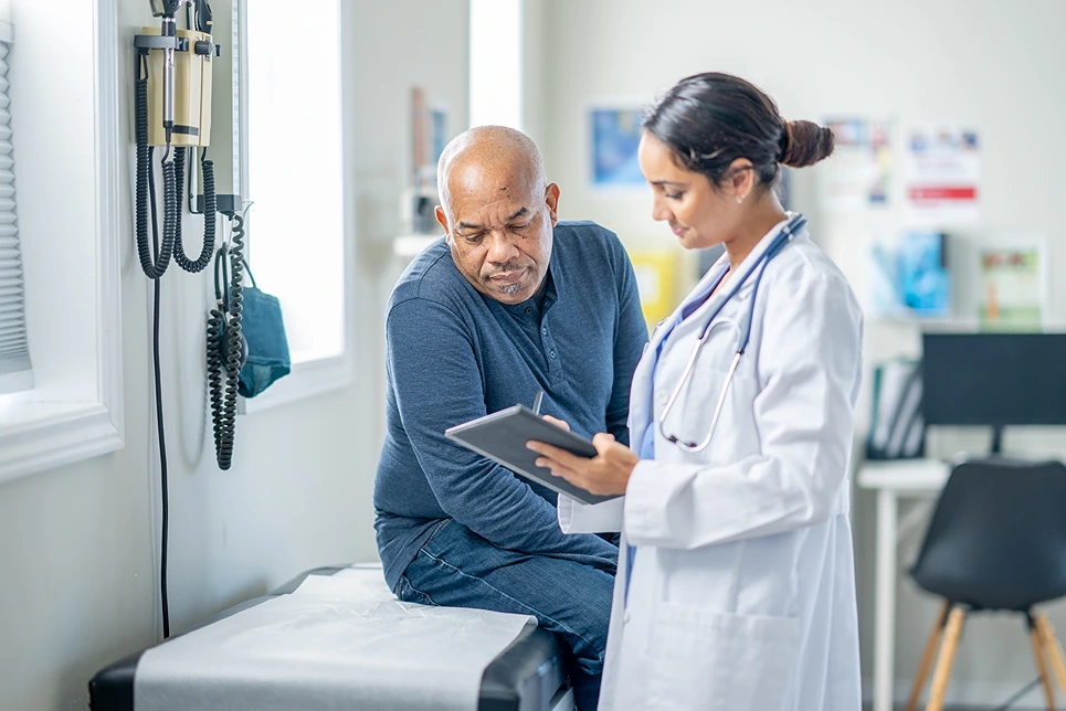 Doctor reviewing medical information on a tablet with a concerned male patient in a clinic office.